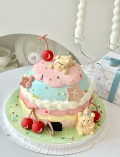 a birthday cake decorated with teddy bears and cherries on a table next to a gift box