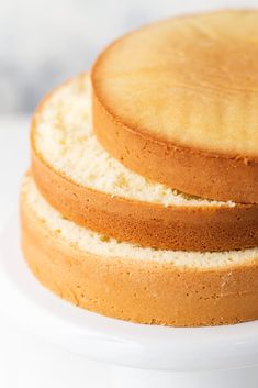 three cakes stacked on top of each other on a white cake plate with one slice cut out