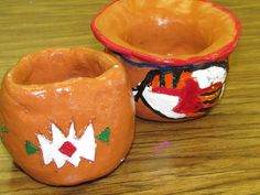 two clay bowls sitting on top of a wooden table next to each other, one painted orange and the other white