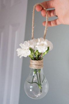 a hand holding a glass vase with white flowers in it and rope wrapped around the bottom