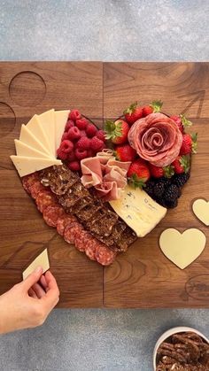 a wooden cutting board topped with cheese, fruit and meats next to a bowl of berries