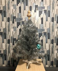 a small silver christmas tree sitting on top of a wooden table next to a wall