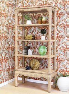 a wicker shelf with books and vases on it in front of a wallpapered wall