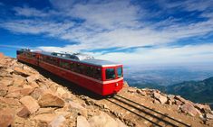 a red and white train traveling on top of a rocky mountain