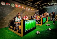 several people are playing soccer on the televisions in a room with green carpet and artificial turf