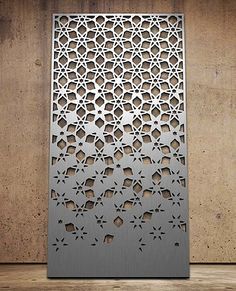 an intricate laser cut metal screen on a wooden floor with concrete wall in the background