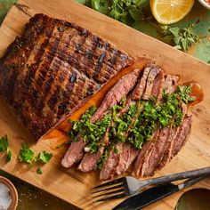 sliced steak on cutting board with garnishes and utensils next to it