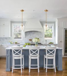 a kitchen with white and blue cabinets, marble counter tops and an island in the middle