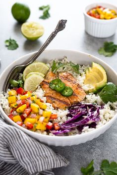 a white bowl filled with rice, chicken and veggies next to limes