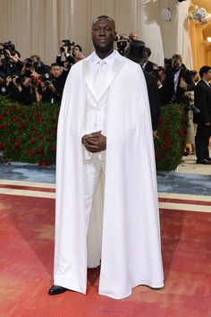 a man in a white suit and cape standing on a red carpet