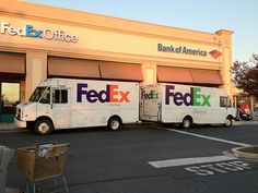 two fed ex trucks parked in front of a bank of america store with the doors open