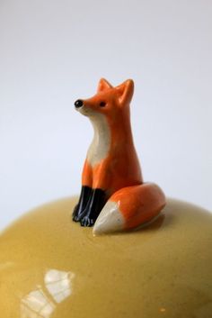 an orange and white fox figurine sitting on top of a yellow vase,