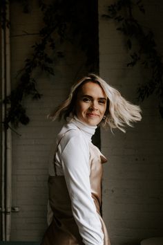 a woman standing in front of a white brick wall with her hair blowing in the wind