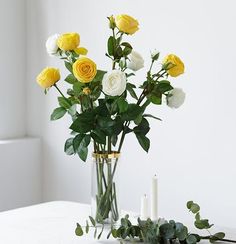 a vase filled with yellow and white flowers on top of a table next to a candle