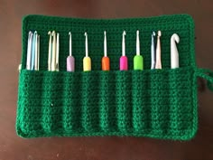 a green crocheted case with six different colored toothbrushes in it on a table