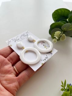 a pair of white earrings sitting on top of a piece of paper next to a plant