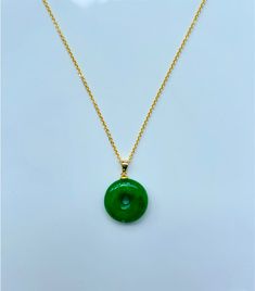 This elegant jade circle necklace features a delicate 18k gold plated chain that gracefully holds a vibrant green jade donut pendant. The rich green hue of the jade contrasts beautifully with the warm gold, creating a timeless and contemporary piece. Perfect for adding a touch of sophistication to any outfit, this necklace is a versatile accessory that can be worn for any occasion. The smooth, polished surface of the high-quality green round jade pendant adds a touch of natural beauty, while the Jade Clavicle Chain With Round Pendant, Dainty Gold Chain Round Necklaces, Dainty Round Gold Chain Necklace, Gold Jade Round Pendant Jewelry, Gold Jade Round Pendant Necklace, Green Round Disc Necklace For Gift, Gold Jade Necklace With Round Pendant, Gold-plated Round Emerald Necklace, Gold Plated Round Emerald Necklace