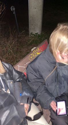 two people sitting on a bench at night with their cell phones in front of them