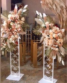 two tall metal vases with flowers and feathers on them in front of a mirror