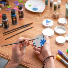 a person holding a paintbrush in front of some art supplies on a wooden table