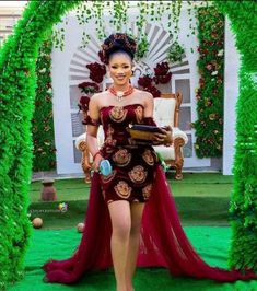 a woman in a red and gold dress is walking through an archway with greenery