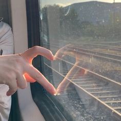 a person making a heart shape with their hands on a train window sill as they look out the window