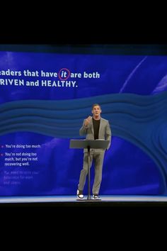 a man standing at a podium giving a speech in front of a blue screen with words on it