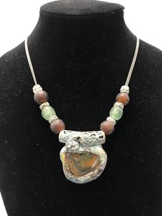 A nice thick piece of glass found in Sri Lanka is framed in patinaed and painted resin.  African glass beads and patinaed metal beads are strong on a double nickel free chain Each Wearable Slip piece is a unique work of art created  and signed by Fredian Slips Unique Patina Round Pendant Necklace, Bohemian Recycled Glass Necklaces For Jewelry Making, Unique Recycled Glass Round Bead Necklaces, Unique Recycled Glass Round Bead Necklace, Artisan Glass Necklaces For Healing, Artisan Beaded Necklaces With Recycled Glass, Artisan Resin Pendant Jewelry, Artisan Soldered Round Beads Jewelry, Bronze Czech Glass Necklace For Jewelry Making