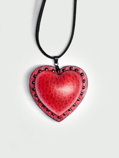 a red heart shaped pendant on a black leather cord with beads and studded edges