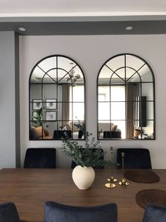 a dining room table with chairs and two large mirrors on the wall over it's windows