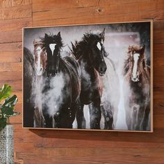 three horses running in the snow on a wood paneled wall behind a vase with a potted plant