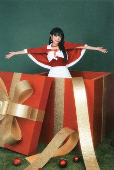 a woman standing on top of a red gift box with gold ribbon and bows around it