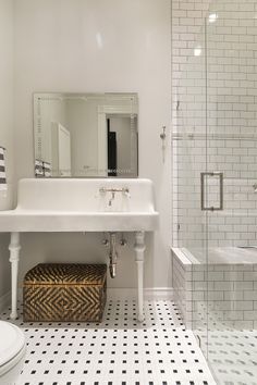 a white bathroom with black and white tile flooring, a large mirror above the sink