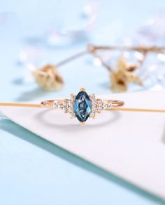 a blue diamond ring sitting on top of a piece of paper next to some flowers