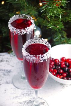 two glasses filled with red liquid next to a bowl of cranberries