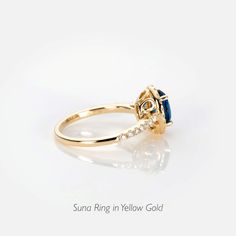 a yellow gold ring with an oval blue stone and diamonds in the center, on a white background