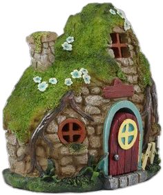 a small house made out of stone with green grass on the roof and door, surrounded by flowers