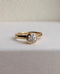 a gold ring with a single diamond on top of the band, sitting on a white surface