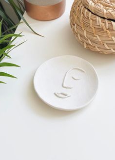 a white plate with a face on it next to a potted plant and a wicker basket