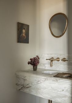 a bathroom with marble counter top and gold faucet, sink and painting on the wall