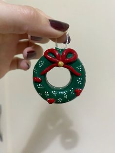 a hand holding a green christmas wreath ornament with red bows and bells on it