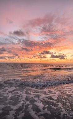 the sun is setting over the ocean with waves coming in to shore and some clouds