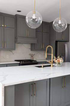 a kitchen with gray cabinets and marble counter tops, two pendant lights over the sink