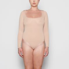 An ultra-chic and flattering long sleeve bodysuit that is made to be a staple in your wardrobe. Features a raw cut scoop neckline and a light level of compression. Lined Scoop Neck Bodysuit For Loungewear, Fitted Bodysuit With Thumbholes And Scoop Neck, Fitted Scoop Neck Bodysuit With Thumbholes, Seamless Second-skin Long Sleeve Bodysuit, Long Sleeve Second-skin Smoothing Bodysuit, Fitted Seamless Bodysuit For Fall, Seamless Fitted Bodysuit For Fall, Seamless Long Sleeve Leotard With High Stretch, High Stretch Seamless Long Sleeve Leotard