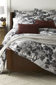 a bed with floral comforter and pillows on top of it next to a night stand