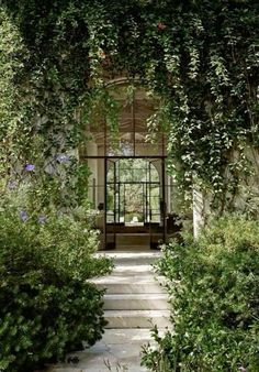 an entrance to a house covered in vines and flowers with a bench on the other side