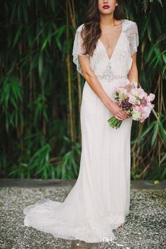 a woman in a wedding dress holding a bouquet and posing for the camera with bamboo trees behind her