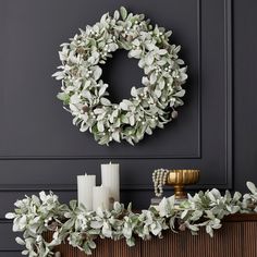 a wreath and candles sit on top of a mantle in front of a gray wall