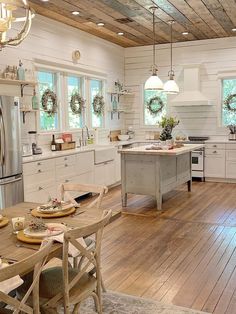 a kitchen with wooden floors and white walls, surrounded by wood flooring the center island has wreaths hanging on it