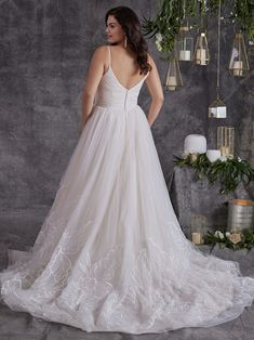 a woman in a white wedding dress standing next to a wall with candles and greenery